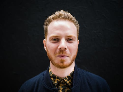 Man smiling looking at camera red hair and beard black background