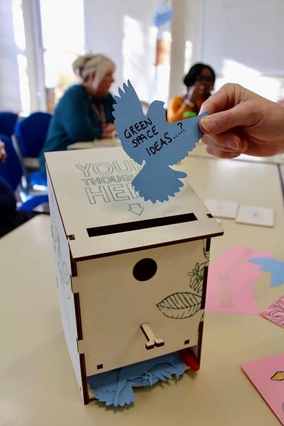 Hand holding bird-shaped note with 'green spaces ideas' on it and bird box