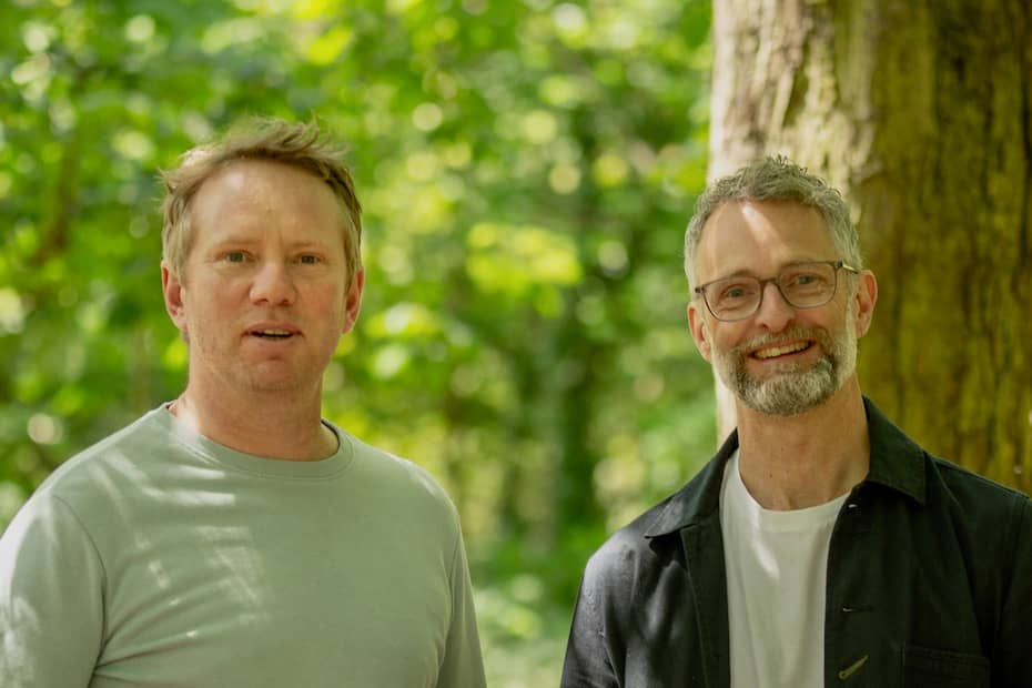 Two white men standing in woodland smiling